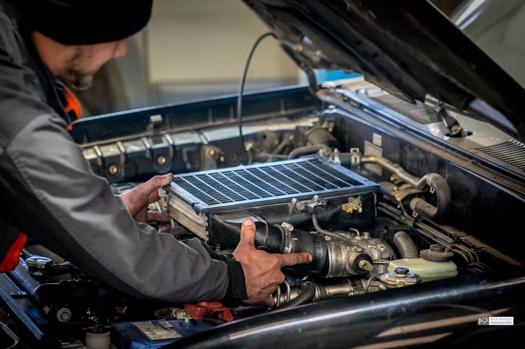 Mécanicien installant un échangeur air-air sur le moteur d'une voiture, mains posées sur l'équipement.