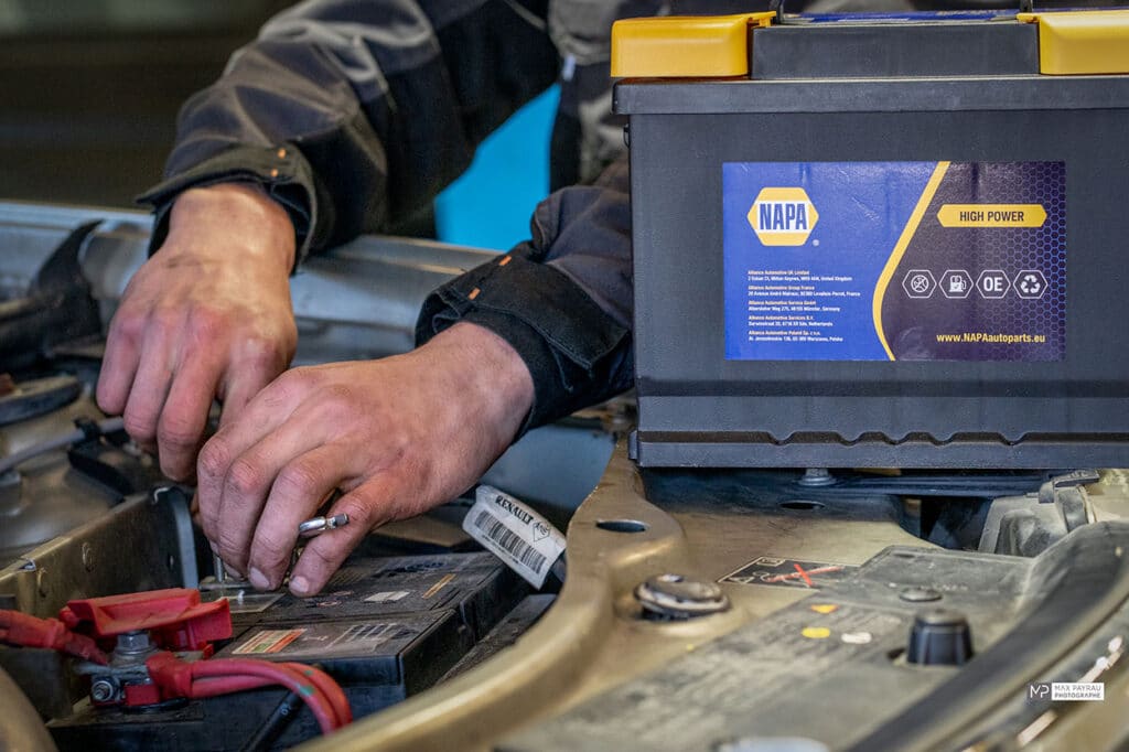 Mécanicien remplaçant une batterie de voiture Renault à côté d'une batterie NAPA High Power prête à être installée.